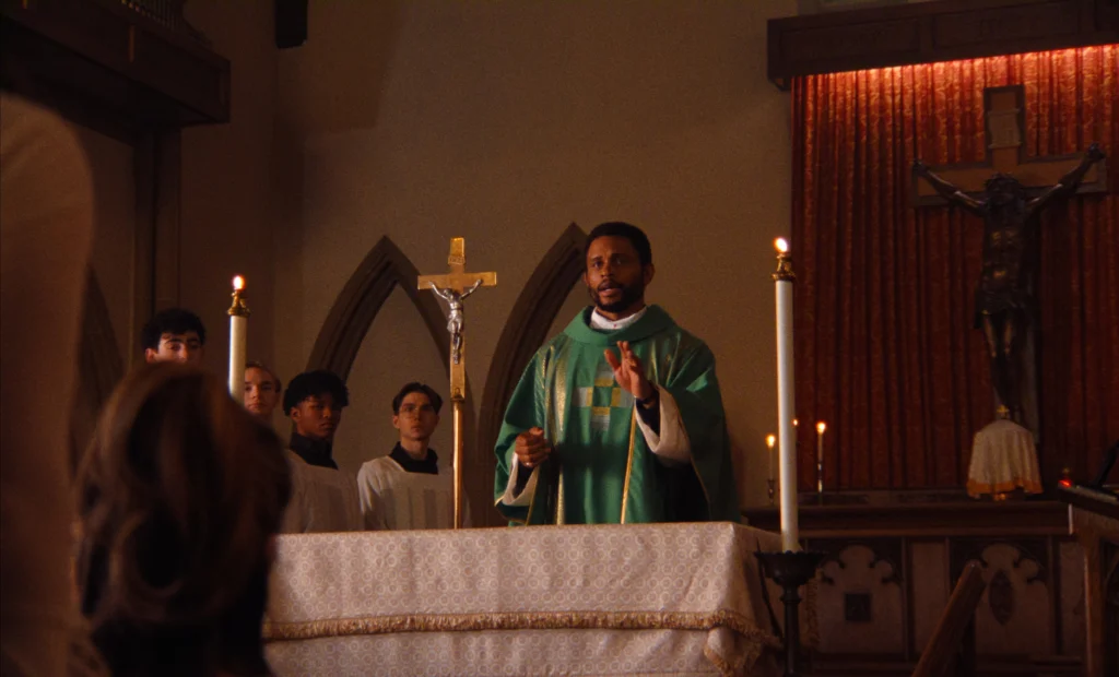 "A priest in green vestments leads a church service at the altar, with altar servers behind him, candles and a crucifix present, and congregants visible in the foreground within a dimly lit sanctuary."