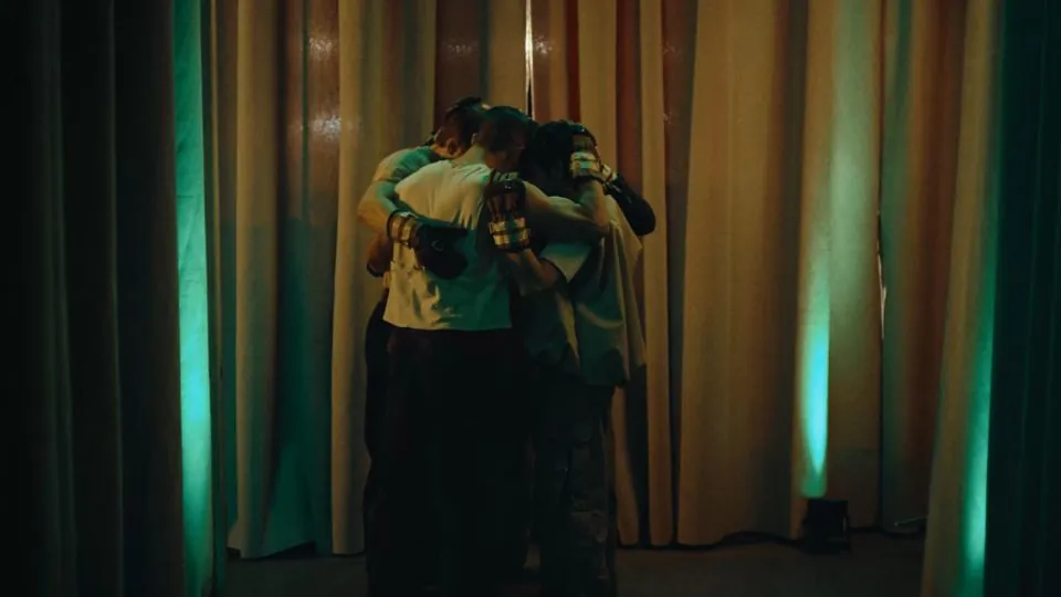 A still from Andrew Hebert's FOUR ITCHY BOYS. Four young men in a dark room huddle together in an embrace.