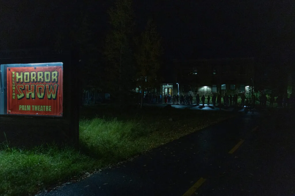 A line at night, and an illuminated sign that reads Telluride Horror Show.