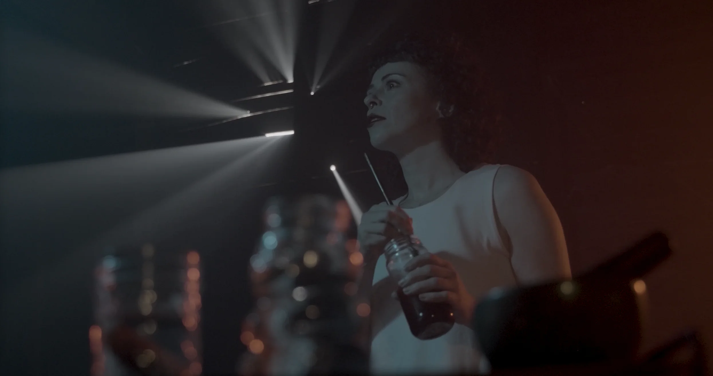 Caitlyn Hamilton in THE CRITIC: a soft-lit image of a woman mixing paint in a jar, staring intently off-screen, as light comes in through a boarded-up window